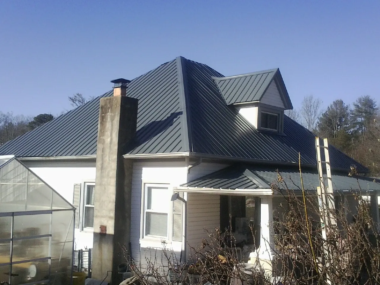 Dark blue standing seam metal roof on a white farmhouse with dormer — Slate & Tile Roof Repair by Roofing Brothers in South Pittsburg