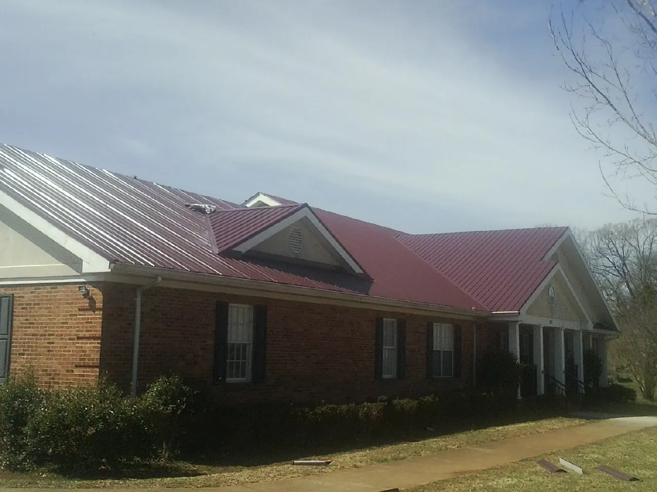 Red metal roof with gabled entries on a long brick building, from a Hail Damage Roof Repair job in South Pittsburg