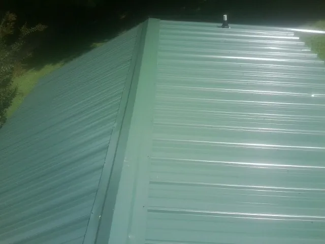 New green metal panels meeting at the ridge of a roof — Flat Roof Repair work by our crew in South Pittsburg