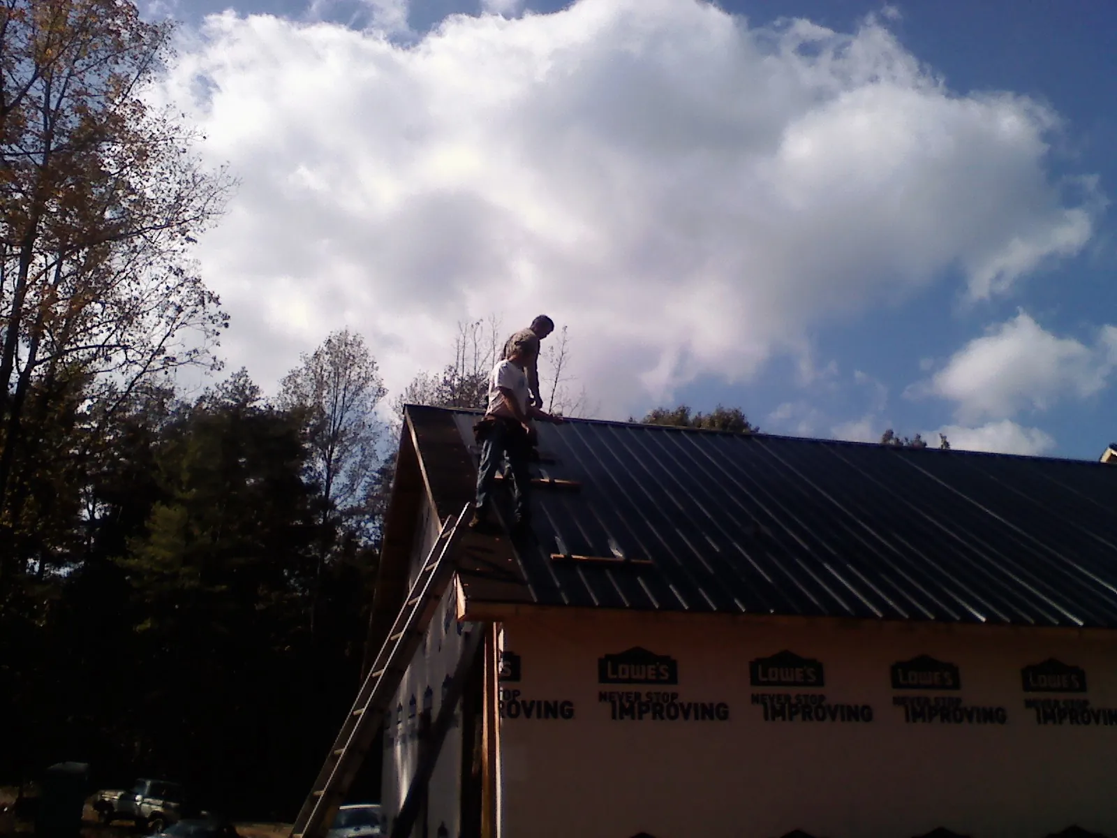 Roofer fastening dark metal panels high against a cloudy sky, from a Roof Inspection job in South Pittsburg