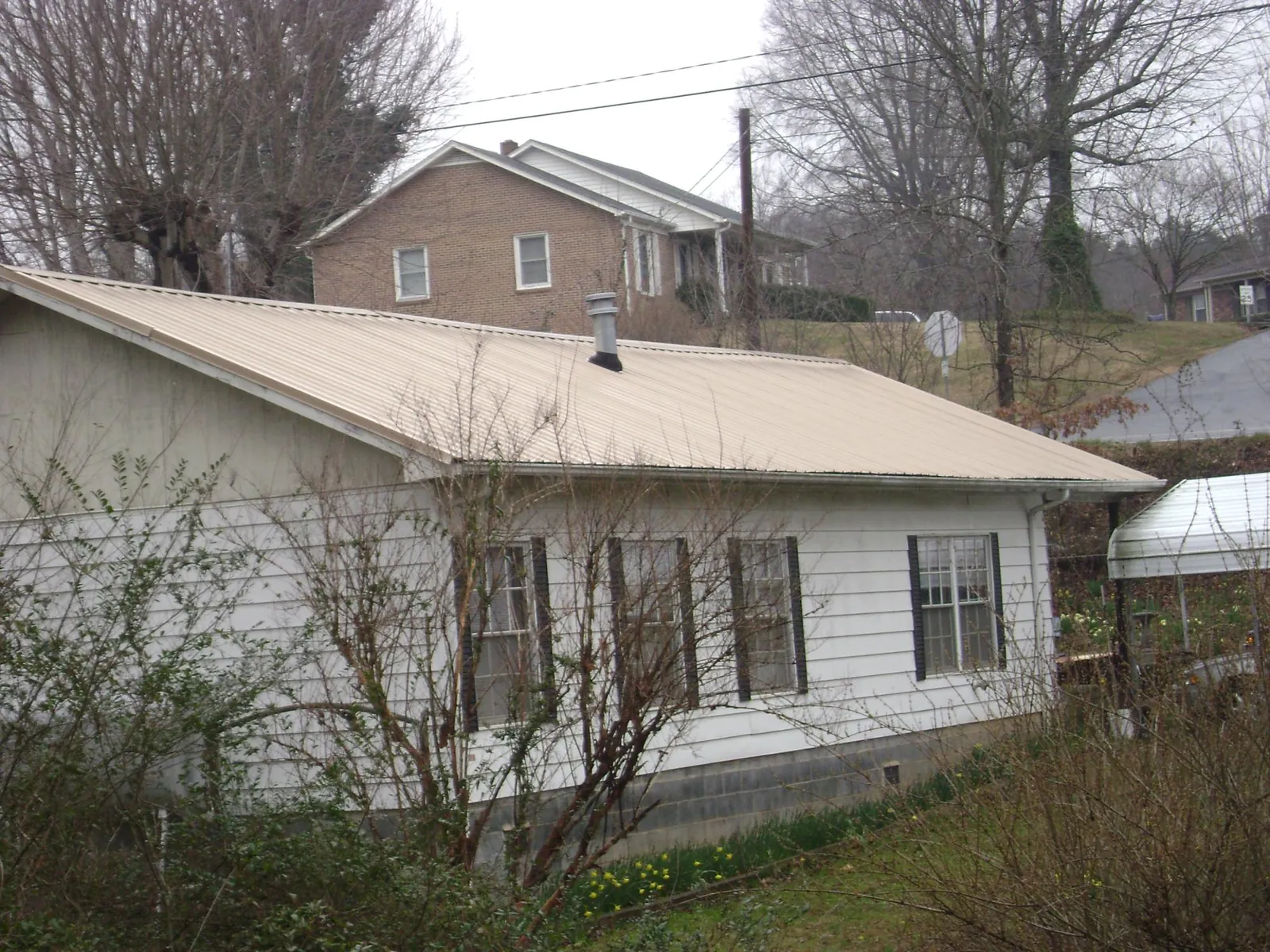 Tan metal roof on a white sided house set into a hillside — Commercial Roofing by Roofing Brothers in South Pittsburg
