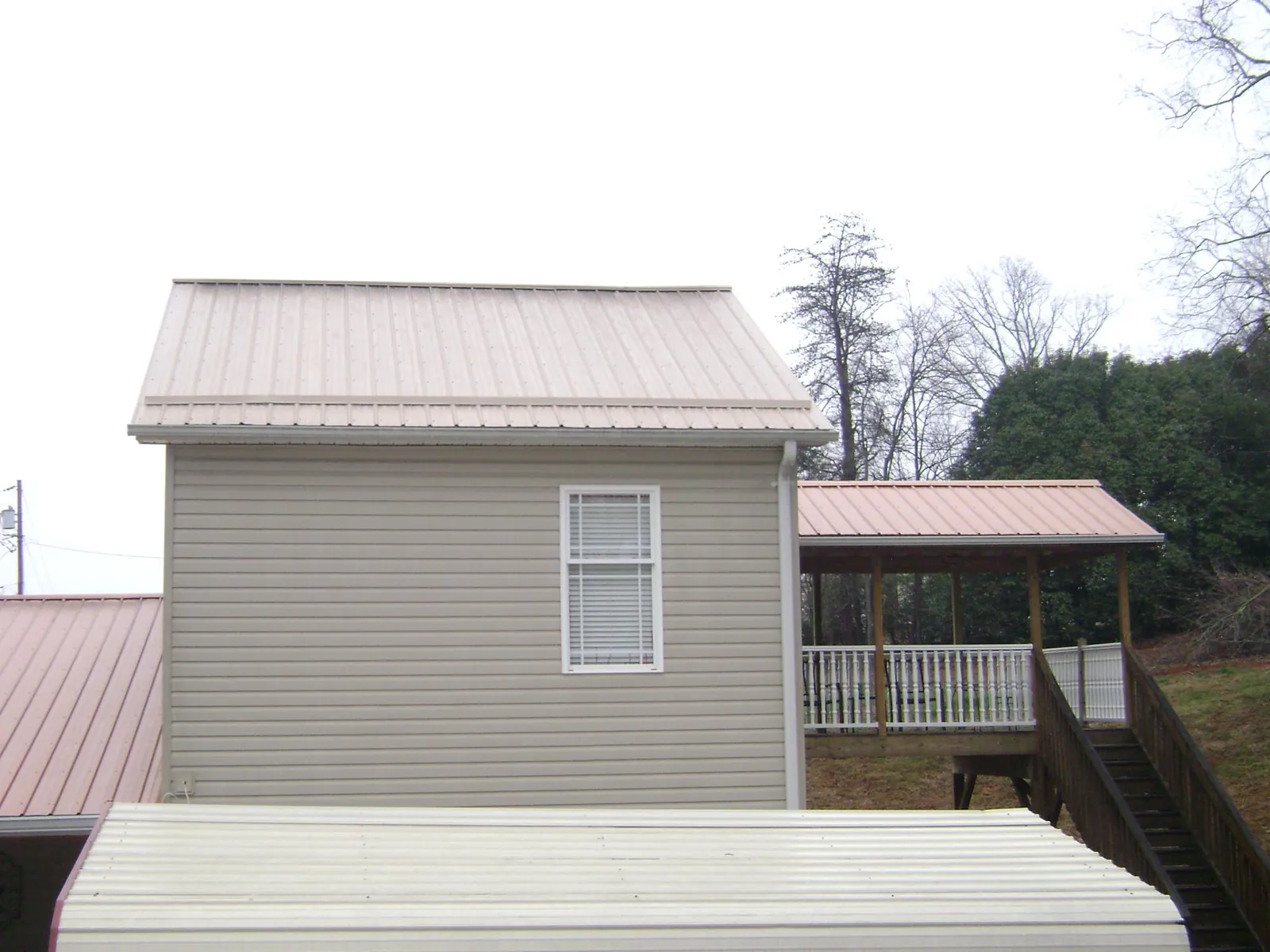 Tan metal roofs on a two story addition and attached porch, from a Roof Replacement job in South Pittsburg